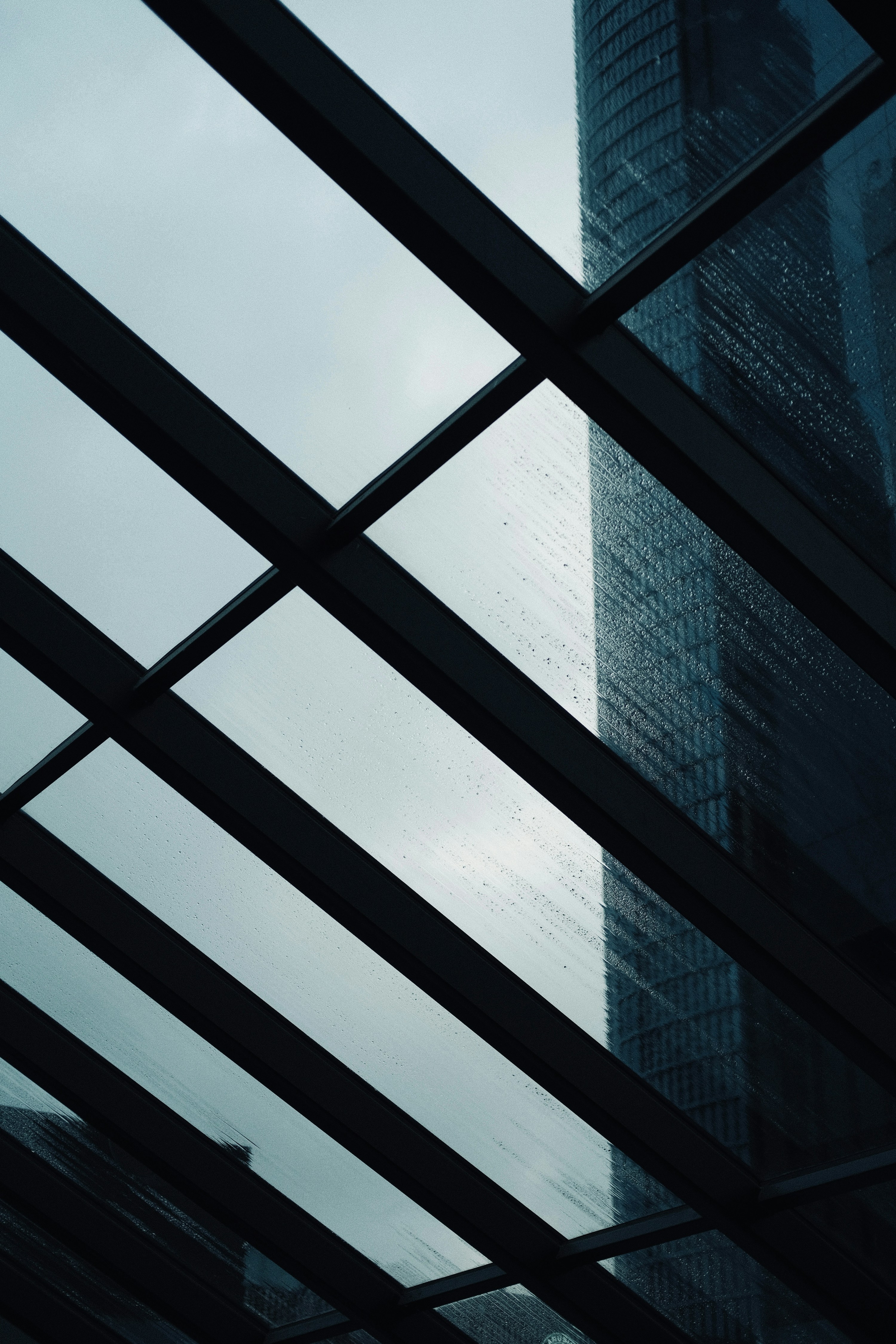 A real steel-and-glass architectural framework seen through rain, with a modern building beyond